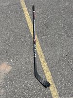 Full view of the CCM JetSpeed hockey stick showing the stick's shaft and blade, placed on asphalt with yellow road stripes.