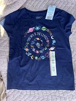 Photo of navy blue kids T-shirt laid flat showing front with colorful space design and tags