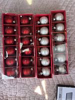 Two red boxes, one containing 12 red mini round Christmas ball ornaments with glittery swirl design, the other containing 12 silver mini round Christmas ball ornaments with glitter swirl pattern.