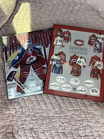 Two framed posters laid on a quilted beige surface showing Patrick Roy in Colorado Avalanche uniform and a historical display of Montreal Canadiens jerseys.