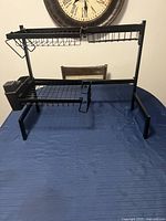 Front view of the black metal over the sink drying rack on a table with clock in background.