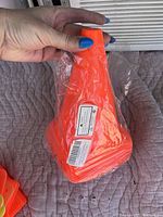 Orange plastic training pylons stacked and wrapped in plastic, held by a hand with blue nail polish, showing packaging and condition.