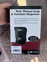 Box of new Rely Manual Soap & Sanitizer Dispenser in black with product details and ADA compliance shown on front.