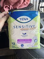 Photo of a sealed package of Tena Sensitive Care incontinence pads held in hand, showing detailed front label and packaging.