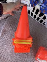 Hand holding a stack of training pylons in orange and yellow colors, plastic cones used for sports training.