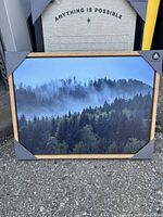 Tree top wall painting with misty forest image in wooden frame on floor with corner protectors.