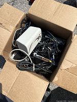 Photo of a cardboard box filled with various used electronic components and cables taken outdoors.
