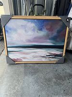 Framed wall art painting showing a landscape scene with pastel colors and wooden frame protected with corner guards.