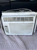 White Noma window air conditioner unit with horizontal vents, control panel, and power cord, showing wear and dirt signs, placed on a gray cloth.