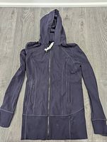 Front view of black fitted Lululemon zip-up hooded jacket laid flat on grey wood floor
