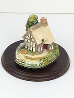 Front angled view of the Blacksmith cottage figurine on wooden base showing front, roof, and garden details.