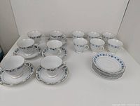 Two sets of teacups and saucers displayed with gold and silver floral detailing, total 23 pieces.