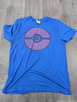 Front view of electric blue t-shirt showing large purple Pokeball graphic in middle