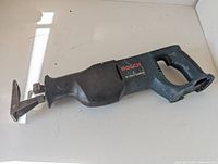 Bosch 18V reciprocating saw with worn paint and cosmetic damage to the plastic body, photographed from the side showing the handle and blade clamp area.