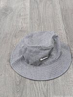Grey Nike bucket hat on wooden floor, shows side view with Nike swoosh logo visible.