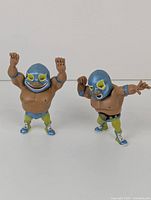 Two El Tabador mascot figurines standing side by side on a white surface, showing full bodies and details of costumes.