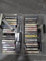Two open plastic cases full of vintage audio cassette tapes laid on dark wood floor. Shows titles and labels of many tapes.