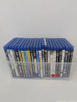 Over 20 Blu-Ray movie discs in their cases set vertically in a clear plastic display holder. Titles visible include 'The Fighter', 'Limitless', and 'Rogue'. Cases appear to be preowned with some minor wear and possible damage.