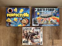 Front view of three classic board games laid out: Perfection, Battleship Outer Space, and Star Wars Trouble. Boxes show visible signs of wear and slight damage, indicating preowned condition.