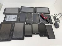 Lot of 16 preowned cellphones and tablets including cracked and intact screens, one red flip phone, and one wired mouse.
