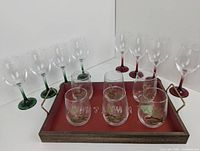 View of all glasses and the serving tray reflecting in a mirror showing colored stemmed wine glasses and stemless reindeer decorated glasses arranged on the tray.