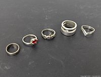 Five sterling silver rings including plain, gemstone, bead design, wide band with clear stone, and V-shaped ring.