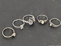 Five sterling silver rings arranged on black background showing various styles and stone settings.