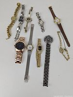 Top view showing all 10 watches arranged in rows on white surface, showing various sizes and band styles including metal link, mesh, chain link, and leather band watches.