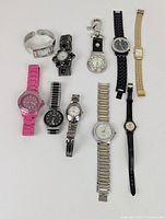 Overview of 10 watches showing varying styles and band materials including plastic, metal links, cuff, leather/synthetic strap. Colors: pink, silver, gold-tone, black. Shows condition and size variety.