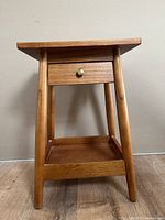 Front view of wooden night stand showing drawer and lower shelf with rounded legs.