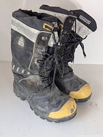 Pair of black and grey insulated winter boots with yellow toe caps and reflective striping, showing slight wear.