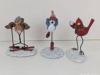 Three bird figurines on snowy bases showing skiing, skating, and snowball throwing poses