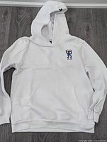 Front view of the white youth hoodie showing the small graphic on the front chest and the kangaroo pocket, hood, and ribbed cuffs.