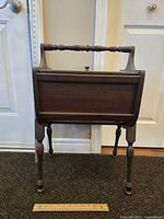 Front view of the antique walnut wooden sewing box showing upright handle, closed double lids, and turned legs with ruler for scale.