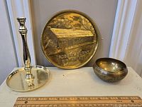 Photo showing the brass candlestick, commemorative plaque, and small bowl with a ruler for size reference.