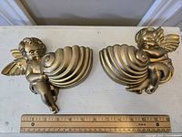 Two gold-tone cherub wall pocket planters side by side with measuring ruler for scale, approximately 10 inches in length each.