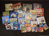 Various children's books on a dark surface, including storybooks, activity books, and board books with colorful illustrated covers.
