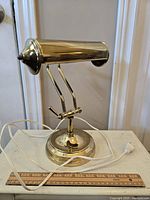 Full view of vintage brass bankers lamp showing cylindrical shade, adjustable arm, round base, and attached power cord.