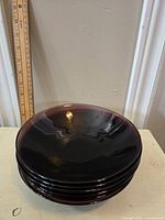 Six amethyst colored glass bowls stacked on a table with a ruler nearby for scale, showing glossy finish and dark purple tone