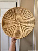 Front view of large round woven basket showing spiral coil pattern and natural fiber texture, held by hand for scale.