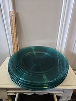 Stack of six large teal glass plates with concentric circle ridges, shown with ruler for scale