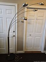 Full view of large heavy chrome floor lamp with 5 light dome-shaped fixtures on arched arms against residential backdrop.