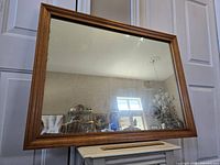 Front view of large rectangular mirror with wood frame reflecting room interior.
