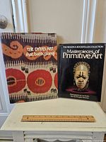 Two hardcover art books placed on a white surface, one featuring colorful traditional textile pattern cover and the other a tribal mask photograph on the cover.
