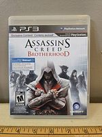 Front cover of Assassin's Creed Brotherhood for PS3 game case, showing title, branding, content notes, and rating.