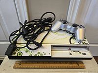 Sony PlayStation 3 console with green and black swirl custom decal skin on white base. Shows front disc slot and power button area, with controller and cables atop console.
