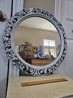 Full view of the round ornate mirror on a table reflecting a room interior