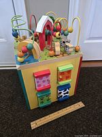 Multicolored wooden toddler activity cube shown from front side with bead maze, sliding blocks, and animal figures