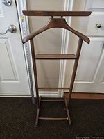 Front view of walnut wood dressing stand showing broad curved hanger and multiple horizontal bars.