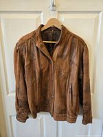 Full frontal view of a brown leather jacket with snap buttons, hanging on a hanger.